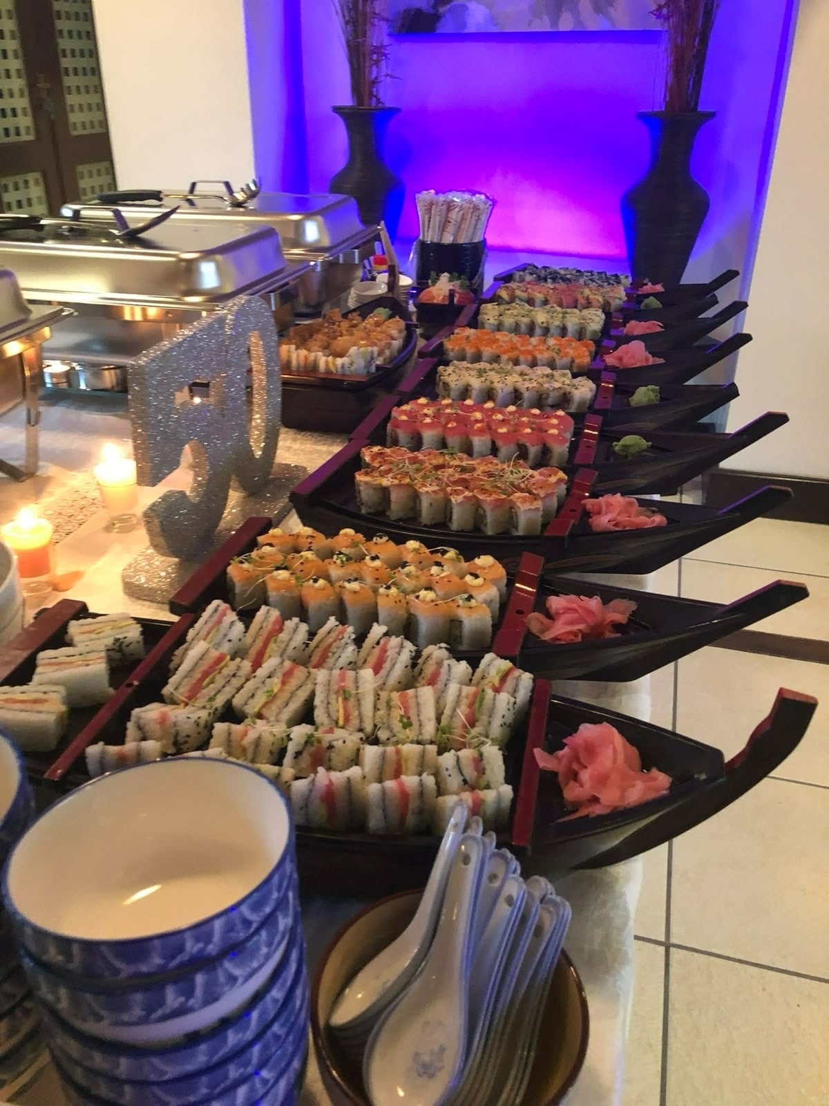 A row of sushi boats, each with ginger and wasabi, on a party table