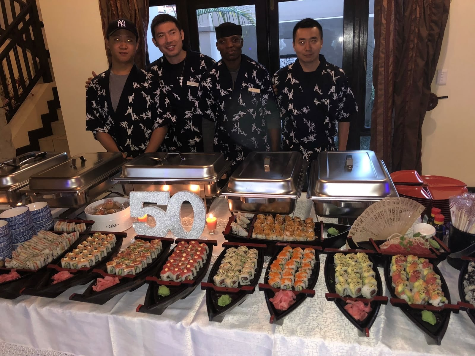 Four Wa Zen chefs behind a long table of sushi boats and chafing dishes